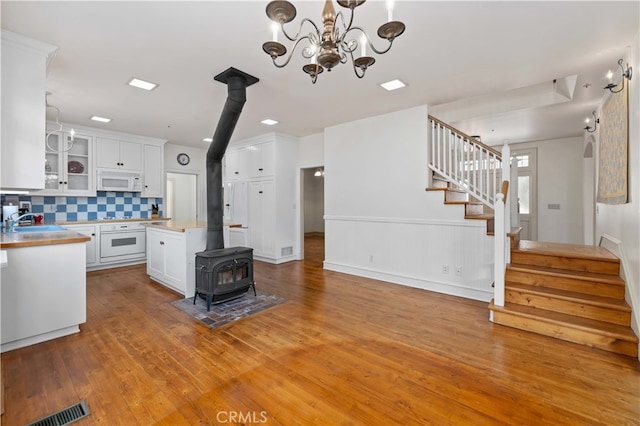 kitchen featuring white appliances, a wood stove, white cabinetry, decorative backsplash, and light hardwood / wood-style flooring