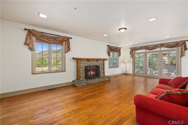 living room featuring a healthy amount of sunlight, a stone fireplace, and hardwood / wood-style floors