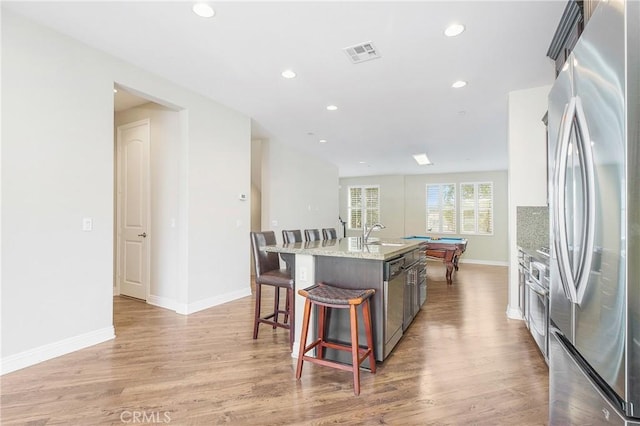 kitchen with billiards, appliances with stainless steel finishes, light hardwood / wood-style floors, and a center island with sink