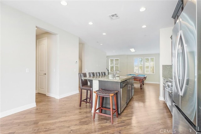 kitchen featuring visible vents, appliances with stainless steel finishes, light wood-style floors, a kitchen island with sink, and baseboards