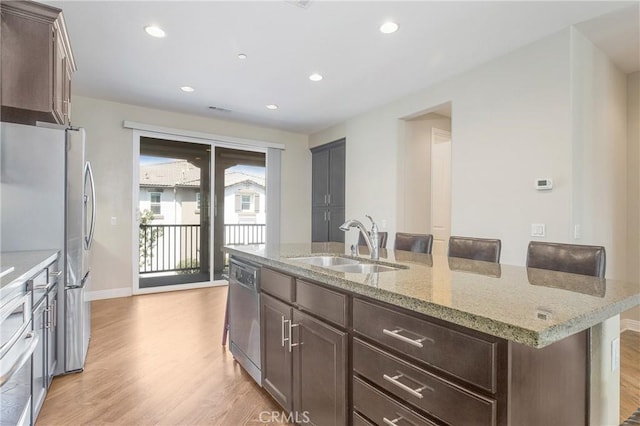 kitchen featuring a kitchen bar, sink, a kitchen island with sink, stainless steel appliances, and dark brown cabinets