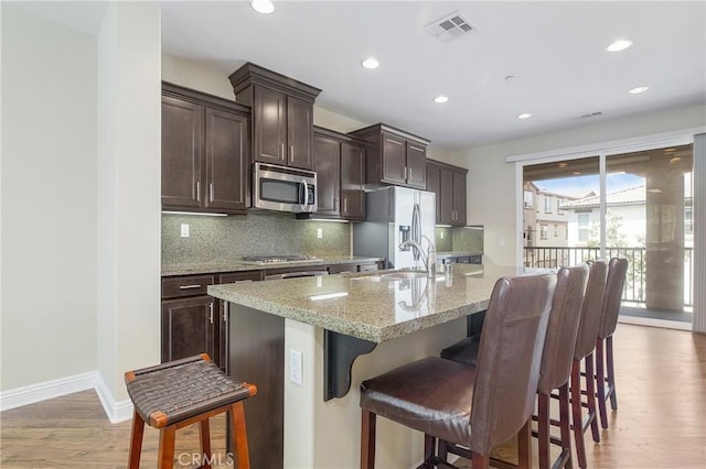 kitchen featuring wood-type flooring, appliances with stainless steel finishes, an island with sink, and a breakfast bar area