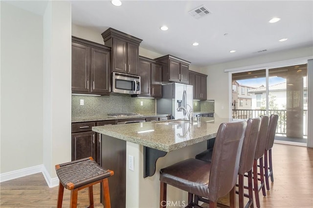 kitchen featuring a kitchen island with sink, a breakfast bar, a sink, visible vents, and appliances with stainless steel finishes