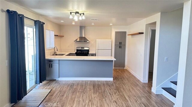 kitchen featuring kitchen peninsula, wall chimney exhaust hood, stainless steel range, sink, and white refrigerator