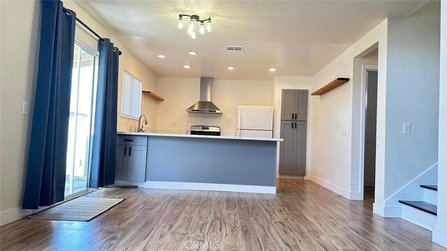 kitchen featuring white refrigerator, a wealth of natural light, wall chimney exhaust hood, and stainless steel range oven