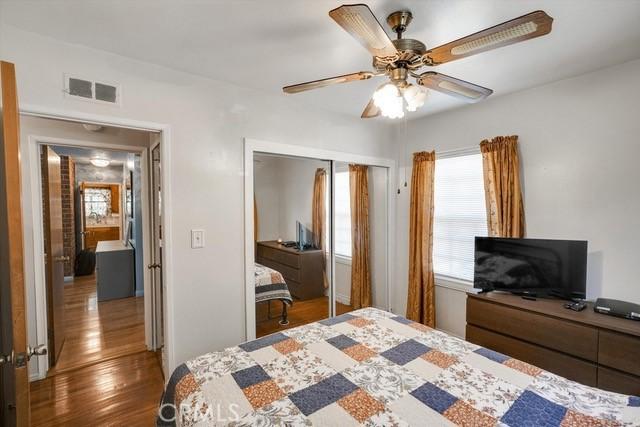 bedroom with a ceiling fan, wood finished floors, visible vents, and a closet