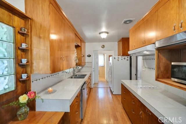 kitchen with visible vents, under cabinet range hood, brown cabinets, stainless steel appliances, and a sink