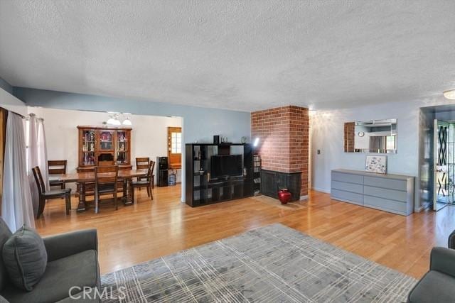 living room featuring a fireplace, a textured ceiling, an inviting chandelier, and wood finished floors