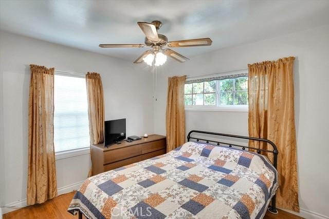 bedroom featuring baseboards, multiple windows, wood finished floors, and a ceiling fan