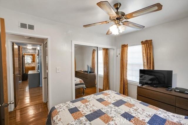 bedroom with a ceiling fan, wood finished floors, visible vents, and a closet