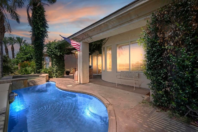 pool at dusk with an in ground hot tub and a patio