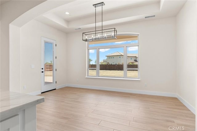 unfurnished dining area with a raised ceiling and light hardwood / wood-style flooring