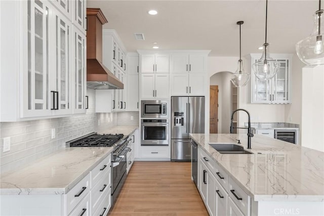 kitchen with sink, hanging light fixtures, wall chimney exhaust hood, white cabinetry, and stainless steel appliances