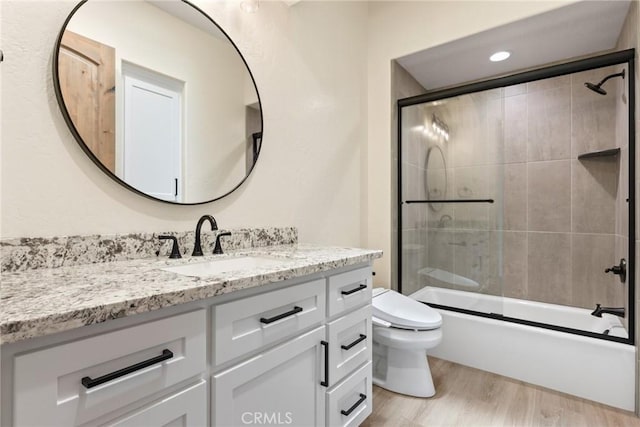 full bathroom featuring hardwood / wood-style floors, combined bath / shower with glass door, toilet, and vanity