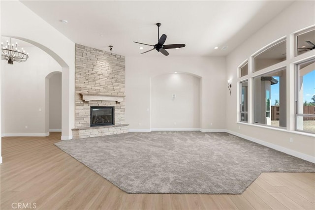 unfurnished living room featuring ceiling fan with notable chandelier, a fireplace, and light hardwood / wood-style flooring