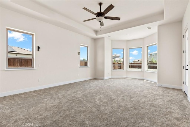 interior space with ceiling fan, a raised ceiling, light carpet, and a wealth of natural light