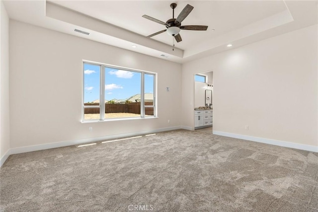 carpeted empty room with ceiling fan and a raised ceiling