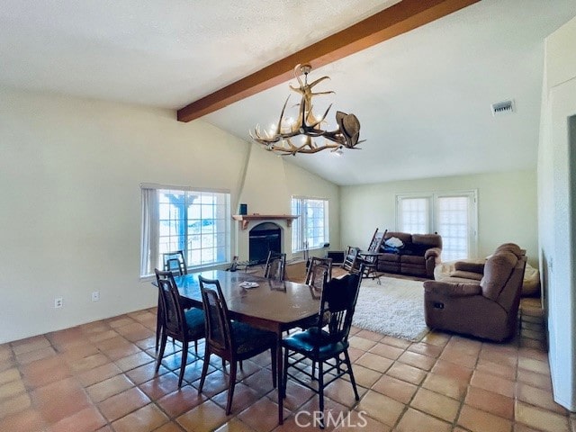 dining space with a healthy amount of sunlight, light tile patterned floors, lofted ceiling with beams, and a fireplace