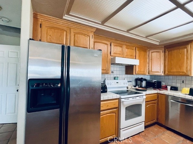 kitchen with appliances with stainless steel finishes, tile counters, and backsplash