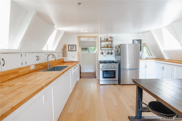 kitchen featuring lofted ceiling, white cabinets, appliances with stainless steel finishes, light wood-type flooring, and sink