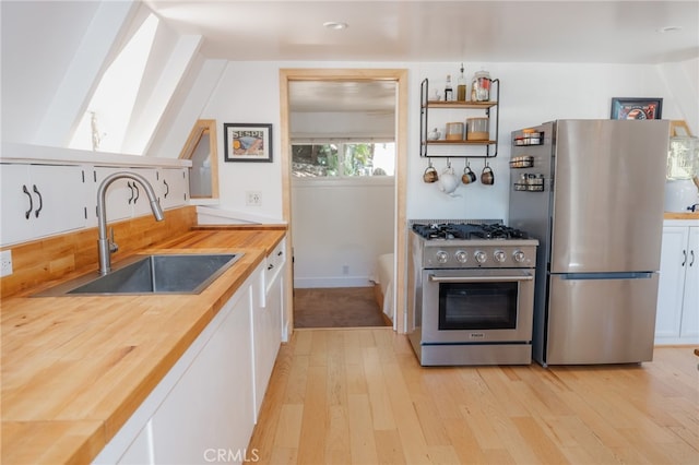 kitchen featuring stainless steel appliances, sink, wooden counters, and white cabinets