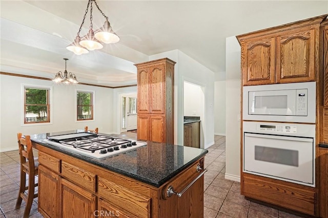 kitchen featuring white appliances, dark tile patterned flooring, a kitchen island, brown cabinets, and pendant lighting