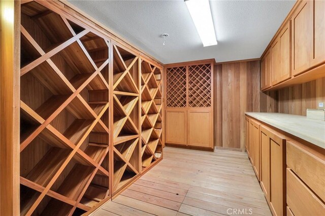 wine cellar with light hardwood / wood-style floors, a textured ceiling, and wooden walls