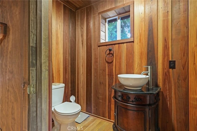 bathroom featuring toilet, wood finished floors, vanity, and wooden walls