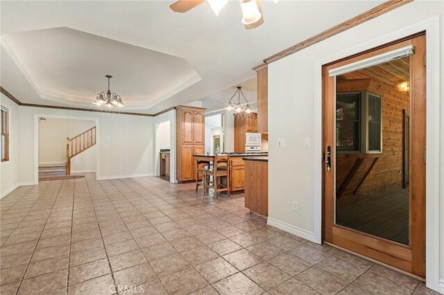 interior space with ornamental molding, wood walls, ceiling fan with notable chandelier, and a raised ceiling