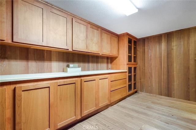 kitchen with light countertops, wooden walls, glass insert cabinets, and light wood-style floors