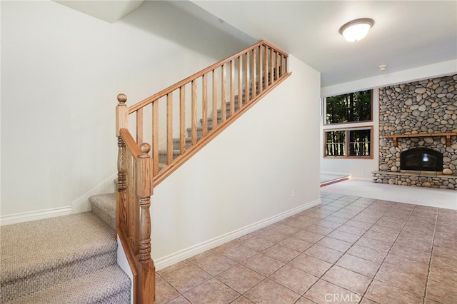 staircase with a stone fireplace and tile patterned floors