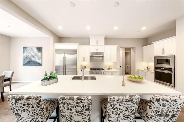 kitchen with a breakfast bar, sink, built in appliances, white cabinets, and a large island