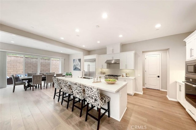 kitchen with a breakfast bar, built in appliances, white cabinetry, and a kitchen island with sink