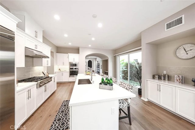 kitchen with white cabinetry, sink, stainless steel appliances, light hardwood / wood-style flooring, and a center island with sink