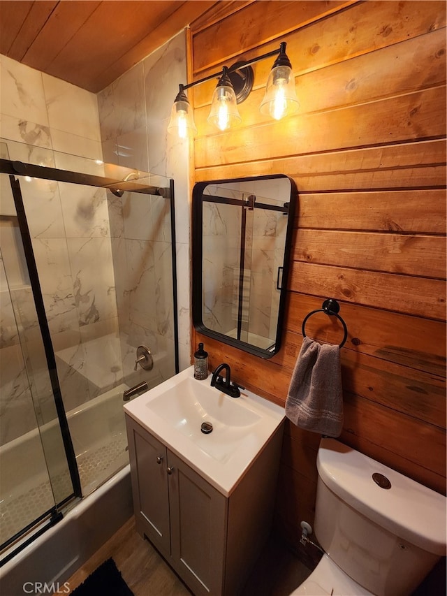 full bathroom featuring vanity, wooden walls, bath / shower combo with glass door, and toilet