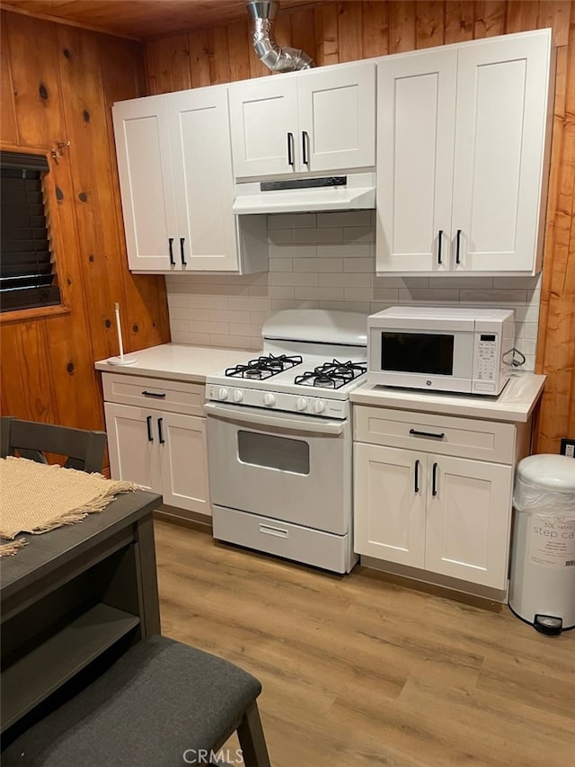 kitchen with wooden walls, white cabinetry, light hardwood / wood-style flooring, and white appliances