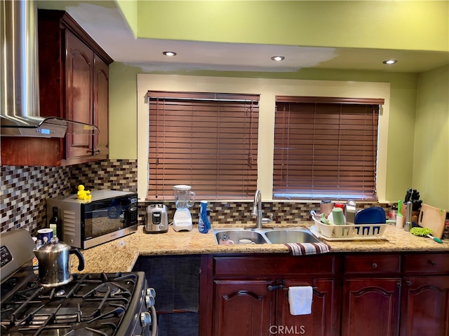 kitchen featuring light stone countertops, appliances with stainless steel finishes, tasteful backsplash, wall chimney exhaust hood, and sink