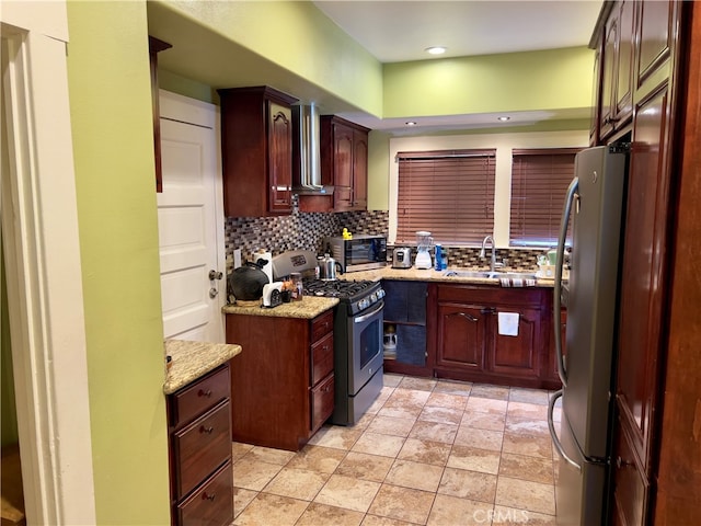 kitchen with backsplash, light stone counters, wall chimney exhaust hood, stainless steel appliances, and sink