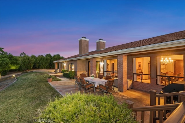 back house at dusk featuring a patio and a yard