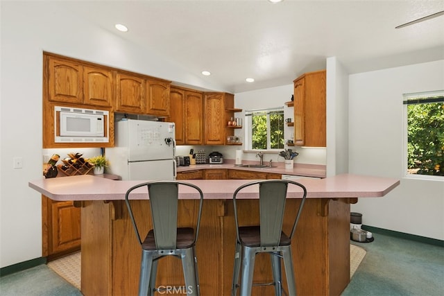 kitchen with sink, a breakfast bar, light colored carpet, and white appliances