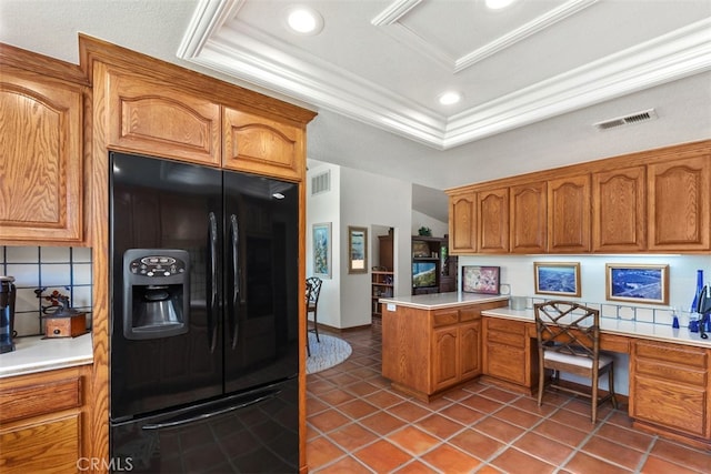 kitchen with built in desk, a tray ceiling, black refrigerator with ice dispenser, dark tile patterned floors, and decorative backsplash