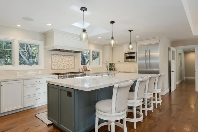 kitchen featuring dark wood-type flooring, hanging light fixtures, a center island with sink, and plenty of natural light