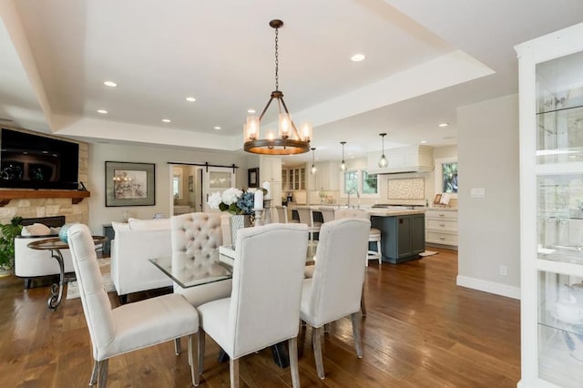 dining space with a raised ceiling, dark hardwood / wood-style flooring, a chandelier, and a barn door