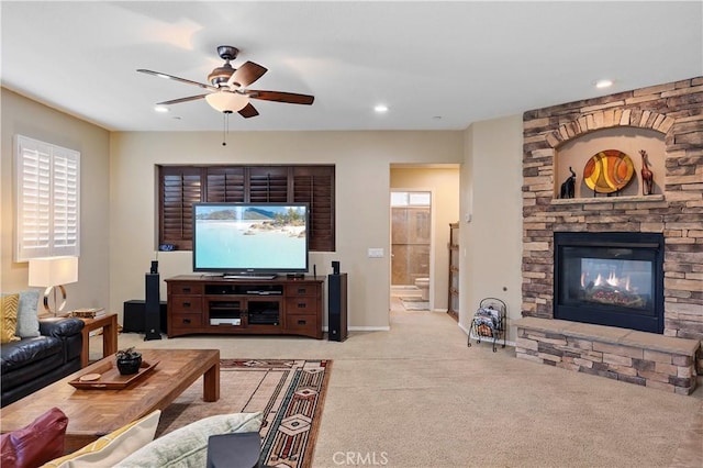 carpeted living area with baseboards, a stone fireplace, recessed lighting, and ceiling fan