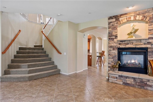 stairs featuring arched walkways, tile patterned flooring, a stone fireplace, and baseboards