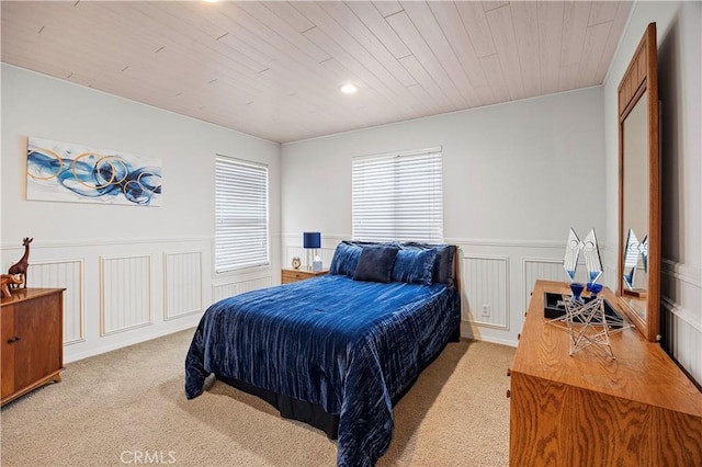 bedroom featuring wainscoting, wood ceiling, a decorative wall, and light colored carpet