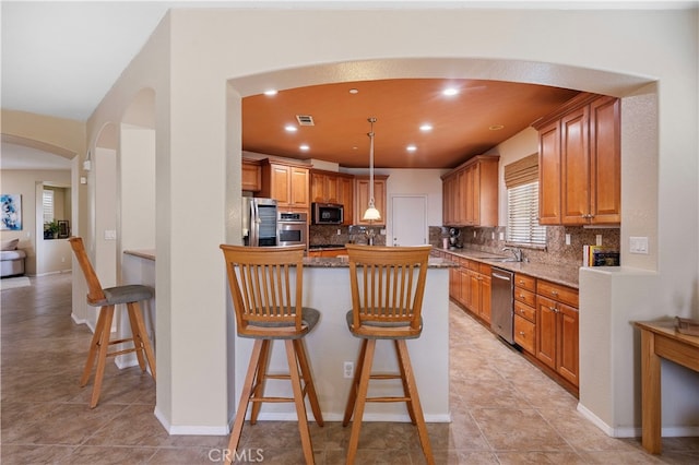 kitchen with tasteful backsplash, appliances with stainless steel finishes, a breakfast bar, sink, and light stone counters