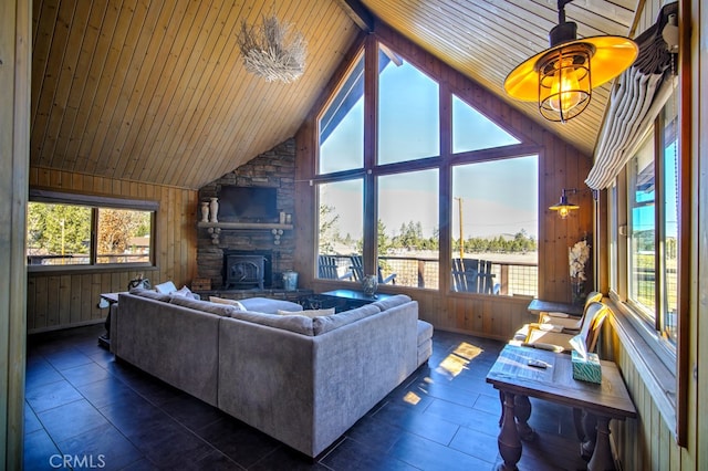 living room featuring ceiling fan, wood walls, a stone fireplace, wooden ceiling, and vaulted ceiling