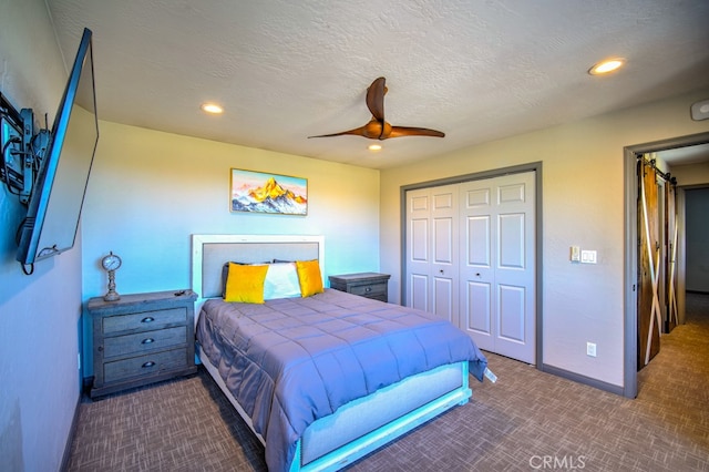 bedroom with a textured ceiling, dark carpet, ceiling fan, and a closet