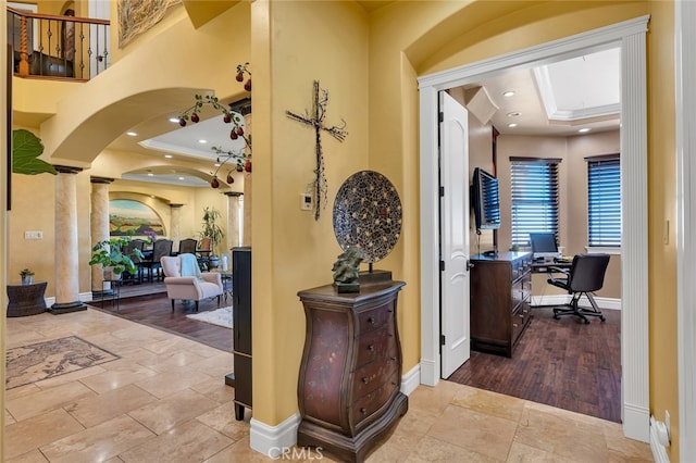 hall with light hardwood / wood-style flooring, decorative columns, and a raised ceiling